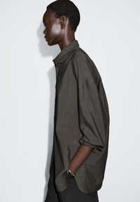 Langarmhemd aus dunkelgrauem Stoff, mit durchgehender Knopfleiste, Kragen und legerer Passform, mit hochgekrempelten Ärmeln und abgerundetem Saum.