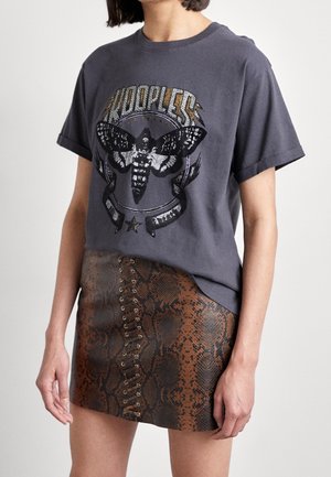 Persona con indosso una maglietta grafica grigio scuro con un disegno di falena e una minigonna marrone con motivo squame di serpente e dettagli frontali con lacci.