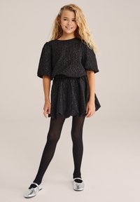 Abito nero con texture, maniche corte e vita elasticizzata, abbinato a collant neri e scarpe slip-on brillanti argento.