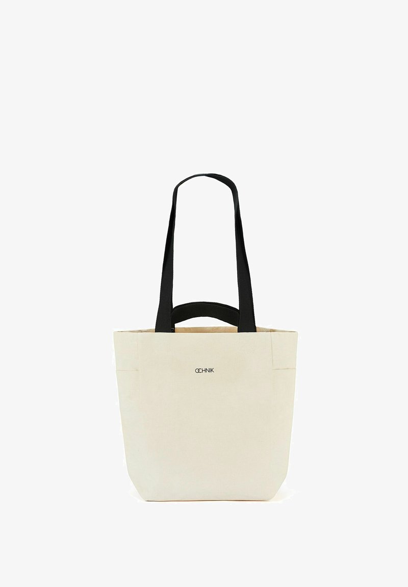 Torebka na ramię z płótna w kolorze off-white z czarnymi uchwytami. Posiada strukturalny kształt, podwójne uchwyty oraz subtelne logo marki z przodu.