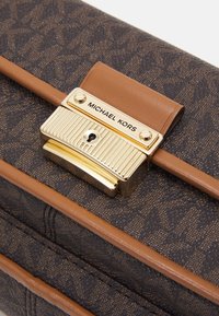 Hnědý texturovaný psaníčko se zlatým a hnědým kováním. Obsahuje zámkovou sponu a je embosováno s logem "MICHAEL KORS".