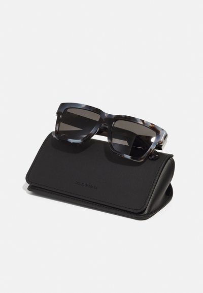Ochelari de soare cu model scoică și lentile închise, așezați pe un capac din piele neagră. Capacul are branding embosat și un design elegant cu pliu.