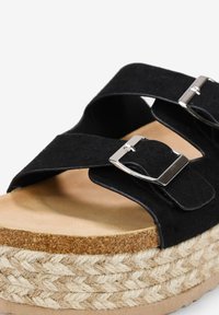 Sandal in suede nero con due cinturini regolabili e fibbie in argento, dotato di una spessa piattaforma intrecciata in juta e una suola liscia beige.