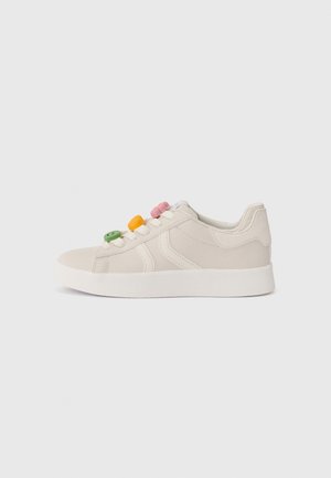 Baskets basses beige avec semelle blanche, ornées de décorations en forme de boutons verts, jaunes et roses sur les lacets, avec détails de coutures latérales.