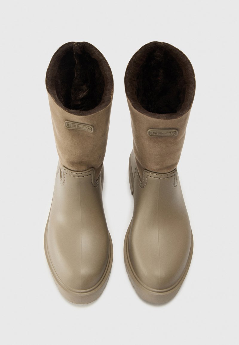Un par de botas de goma beige con un suave forro interno marrón, mostradas desde una vista superior sobre un fondo blanco.