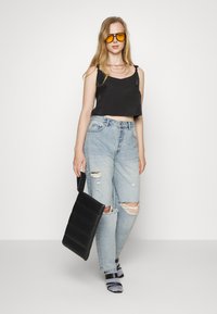 Top cropped preto, jeans rasgados azul claros, mala de ombro preta oversized e óculos de sol com lentes amarelas. Tecido texturizado e ajuste casual.