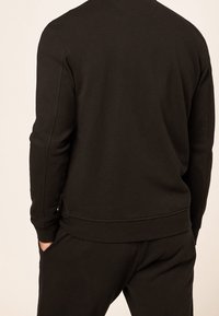 Sudadera negra de mezcla de algodón, con cuello redondo, mangas largas y puños acanalados. Diseño sencillo sin patrones visibles.
