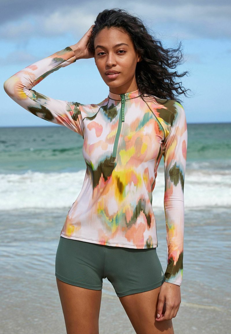 T-shirt de surf à manches longues avec un motif abstrait multicolore dans les teintes de rose, vert et jaune. Présente un col zippé mi-hauteur et un tissu doux et extensible.