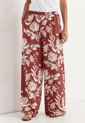 Pantalon à jambes larges avec fond grenat et grand imprimé floral blanc, taille élastique avec cordon, porté avec des sandales noires.