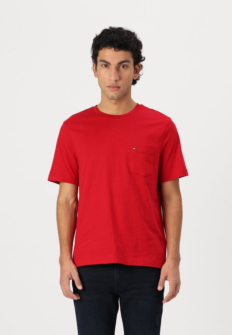 Rød bomulds T-shirt med korte ærmer, rund hals og en lomme på venstre bryst med et lille logodetalje. Glat tekstur.