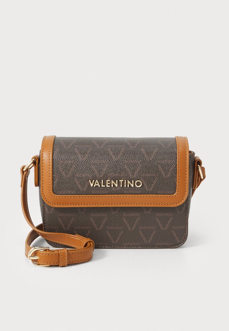 Bolsa crossbody marrom com material texturizado, detalhes em tom bege, acessórios em ouro e fecho com aba apresentando um logótipo. Inclui uma alça ajustável.