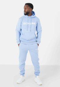 Felpa blu chiaro con la scritta "SIXTH JUNE" stampata in bianco, abbinata a pantaloni jogger coordinati. Realizzata in tessuto morbido, con polsini a coste e tasche.