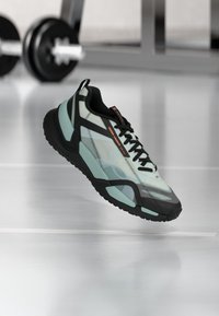 Αθλητικό παπούτσι με ανοιχτό μπαλαντζέ και μαύρο σχεδιασμό, με επάνω μέρος από δίχτυ, υφή σε λαστιχένια σόλα και μαύρα κορδόνια, εμφανιζόμενο στον αέρα.