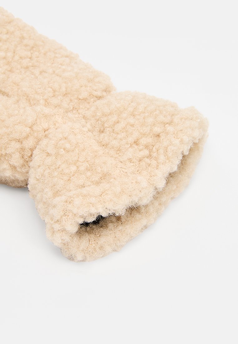 Tejido texturizado beige con apariencia esponjosa, con un borde enrollado. Material suave y grueso, adecuado para la calidez.