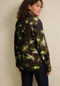 Blusa a stampa floreale in colori scuri, con tonalità di verde e bianco, maniche lunghe, polsini con bottone e orlo curvo. Tessuto trasparente.