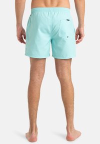 Shorts de bain bleu clair fabriqués en tissu lisse, avec une taille élastique et une poche arrière avec un détail bouton. Ourlet cousu à plat.