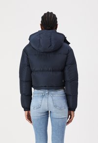 Mørkeblå, kort pufferjakke med hette, med elastiske mansjetter og rundet hem. Glatt, blank tekstur med quiltet mønster.