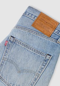 Ανοιχτό μπλε τζιν παντελόνι διπλωμένο, που δείχνει την πίσω τσέπη με την κόκκινη ετικέτα της Levi's και την καφέ δερμάτινη ετικέτα Levi Strauss & Co.