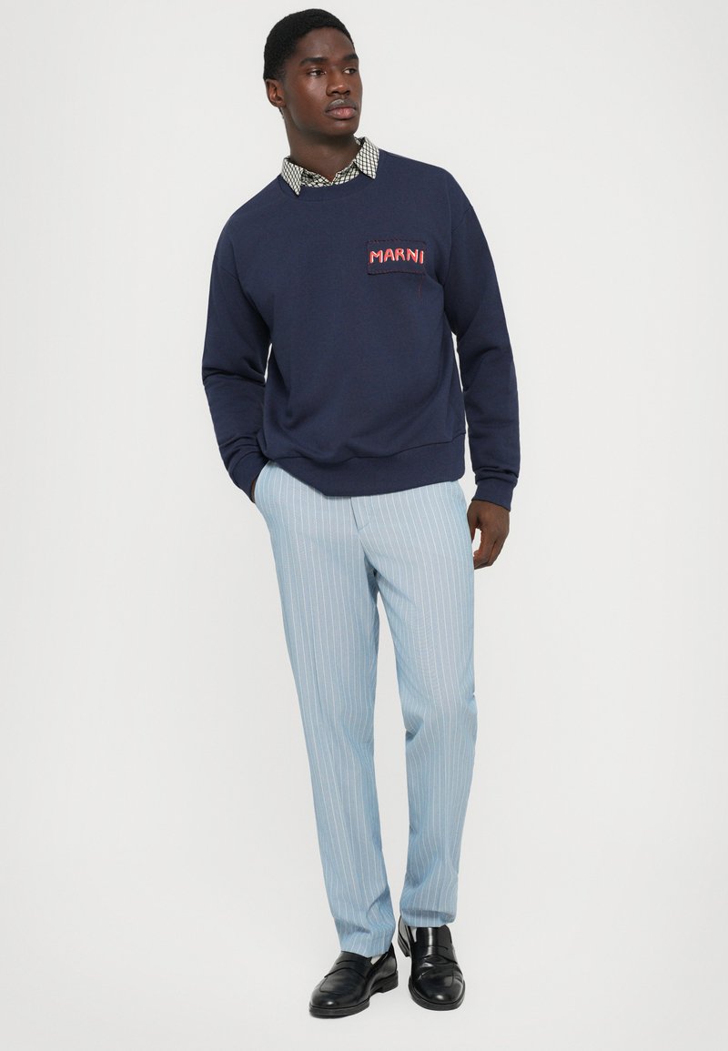 Navy sweatshirt with "MARNI" embroidery, worn over a patterned shirt; paired with light blue pinstriped pants and black dress shoes.