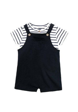 Salopette courte bleu marine avec un t-shirt rayé blanc et bleu marine en dessous. Présente des accents en bois et une poche avant sur la salopette.