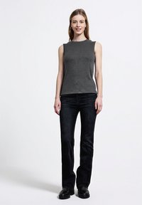 Harmaa ribattuja hihattomia yläosia, yhdistetty tummiin farkkuleveisiin housuihin. Malli seisoo mustissa kengissä yksinkertaisen vaalean taustan edessä.