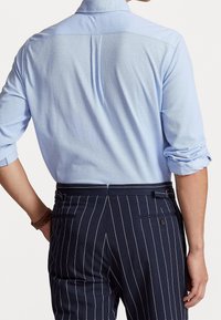 Jasnoniebieska koszula z długim rękawem, z podwiniętymi rękawami, zestawiona z granatowymi spodniami w prążki, posiadającymi tylne kieszenie i dopasowany krój.