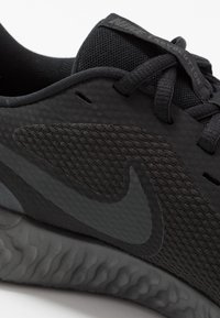 Gros plan sur une chaussure de course Nike noire mettant en avant le mesh texturé, les lacets et la semelle rembourrée avec un motif ondulé.