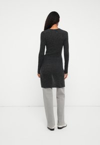 Suéter de tunica de manga longa cinza escuro com silhueta ajustada e barra reta, combinado com calças retas cinza claro e calçado preto.