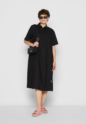 Black short-sleeve dress with a buttoned collar and relaxed fit. Paired with pink sandals and a black bag featuring gold hardware.