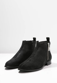 Botines negros con una superficie texturizada y cremallera lateral, exhibidos contra un fondo blanco liso.
