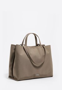 Beżowa torba na ramię wykonana z gładkiego, trwałego materiału. Posiada dwa krótkie uchwyty oraz subtelne logo na przedniej stronie, z otwartym górnym wykończeniem.