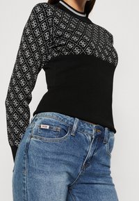 Maglione nero con sezione superiore decorata in bianco e grigio. Presenta una scollatura rotonda e polsini a coste. Abbinato a jeans di denim blu.