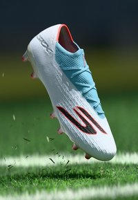 Chuteira de futebol com um design branco e azul claro, superfície texturizada, acentos negros e vermelhos marcantes, e cravos multicoloridos.