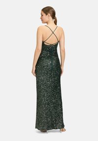 Grünes Pailletten-Abendkleid mit enganliegender Silhouette, kreuzenden Trägern im Rücken und einer Bindeschließe. Langer Schnitt mit glatter Textur.