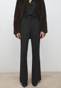 Czarne spodnie na miarę z wysokim stanem i rozszerzanymi nogawkami, wykonane z teksturowanej tkaniny. Noszone z ciemną dopasowaną bluzką i brązowym futrzanym płaszczem.