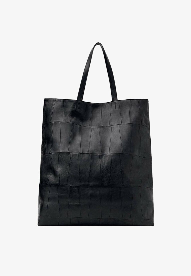 Grand sac cabas en cuir noir avec un design de panneaux cousus et deux fines bretelles, présenté sur fond blanc.