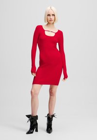 Rochie tricotată roșie cu dungi, cu mâneci lungi, având o decupare pătrată la guler și un accent metalic. Modelul poartă cizme negre cu toc.