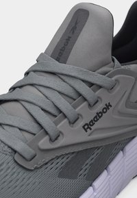 Κοντινό πλάνο γκρι αθλητικού παπουτσιού Reebok με υφασμάτινα κορδόνια υφής, πλεκτό ύφασμα και παχιά λευκή σόλα.
