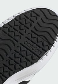 Czarna gumowa podeszwa buta z teksturowanymi wzorami, z białą krawędzią. Na powierzchni wytłoczone słowo "adidas".