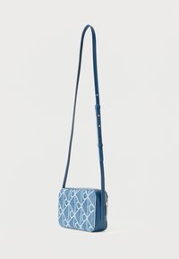 Μικρή ορθογώνια μπλε τσάντα χιαστί με λευκή γεωμετρική κεντητική και ρυθμιζόμενο λουρί ώμου που κρέμεται σε απλό φόντο.