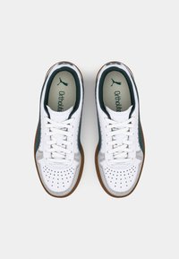 Bílé tenisky se zelenými akcenty, perforovanými detaily a gumovou podrážkou. Obsahují šňůrky a branding "Ortholite" na stélce.