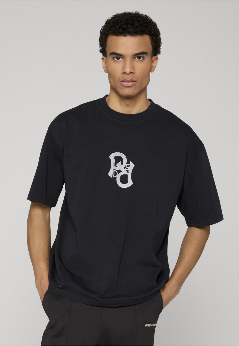 Camiseta negra extragrande de algodón, con un logo blanco estilizado en el pecho y mangas cortas, combinada con pantalones oscuros.