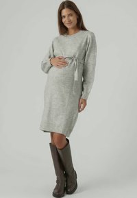 Γκρίζα πλεκτή μίνι φόρεμα εγκυμοσύνης με μακριά μανίκια, ζώνη στη μέση, μήκος ως το γόνατο, συνδυασμένο με καφέ μπότες μίνι. Λείο υλικό, άνετη εφαρμογή.