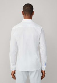 Camisa blanca de manga larga, tela de algodón suave, puños abotonados, collar clásico, detalle de costura trasera y acento de abertura lateral.