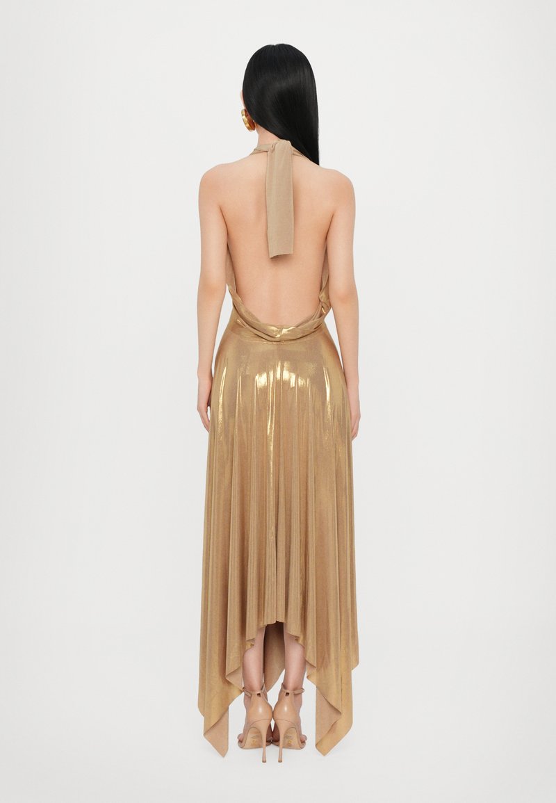 Abito halter in oro metallizzato con schiena bassa, texture plissè e orlo irregolare. Completato con un dettaglio al collo legato e tacchi beige.