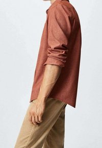 Ruskian värinen, lyhythihainen nappipaita, joka on valmistettu teksturoidusta kankaasta, jossa on käännetyt hihat ja rento istuvuus. Yhdistetty kevyisiin vaaleanruskeisiin samettihousuihin.