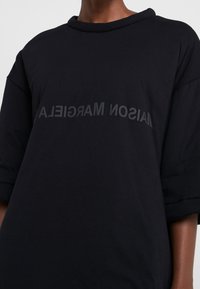 Czarny, oversize’owy t-shirt wykonany z bawełny, z okrągłym dekoltem i opuszczonymi ramionami. Na przodzie tonowany nadruk z napisem „MAISON MARGIELA”.
