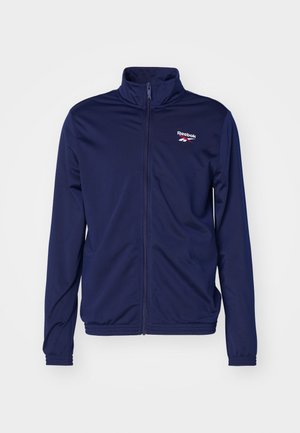 Chaqueta Reebok azul marino con cremallera completa, cuello alto y mangas largas, con pequeño logo en el pecho izquierdo y puños elásticos.