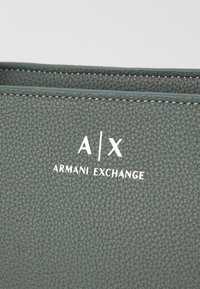 Zeleni teksturirani kožni novčanik s uzdignutim logotipom "A|X ARMANI EXCHANGE" u bijeloj boji, s kontrastnim šavovima.