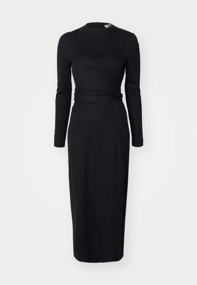 Musta pitkähihainen mekko, jossa on pyöreä kaula-aukko, epäsymmetrinen kietaisumalli ja istuva vyötärö. Valmistettu sileästä, joustavasta kankaasta.